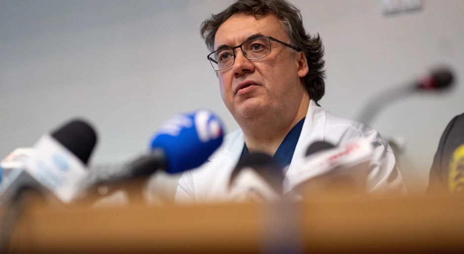 zdjęcie lekarza wypowiadającego się do mikrofonów, przy mównicy drewnianej